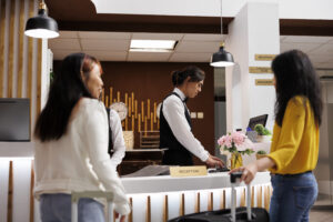Cozy hotel reception with two female guests waiting for concierge to finalize booking procedure. Relaxed customers holding baggages getting ready to check in at lavish resort